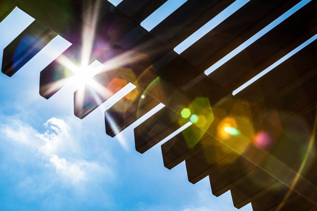 sun shining through the roof of a wooden pergola covering